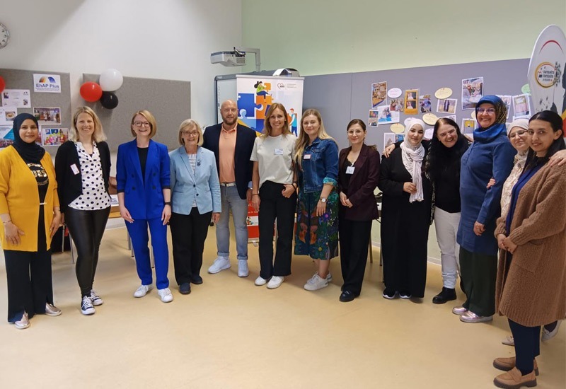 Ein Gruppenfoto mit dreizehn Personen welche im Halbkreis stehen und in die Kamera lachen