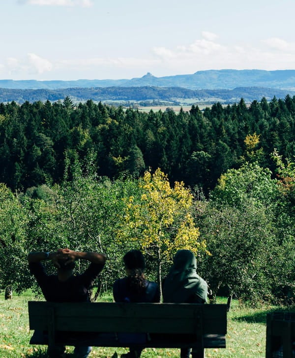 Drei Menschen sitzen auf einer Bank und blicken über Wald und Landschaft in die Ferne