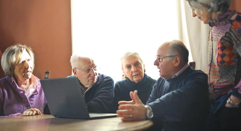 Mehrere Menschen sitzen gemeinsam an einem Tisch mit einem Laptop und sprechen miteinander