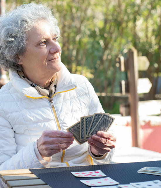Frau sitzt im Freien an einem Tisch und hält Spielkarten in der Hand