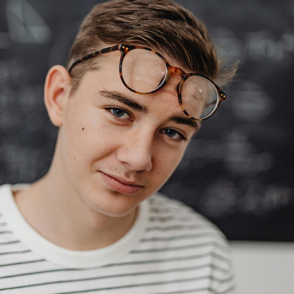 Ein junger, lächelnder Auszubildender mit Brille vor einer Tafel, stellvertretend für die moderne generalistische Pflegeausbildung bei der AWO